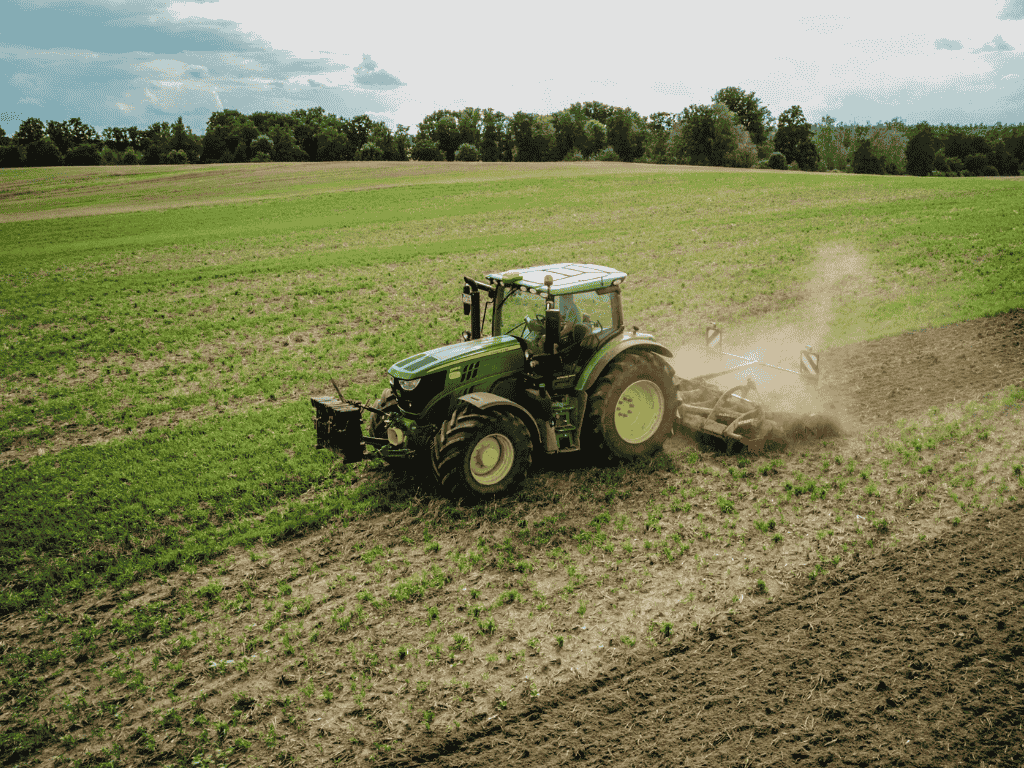 En la imagen se ve un tractor en un prado de producción agrícola